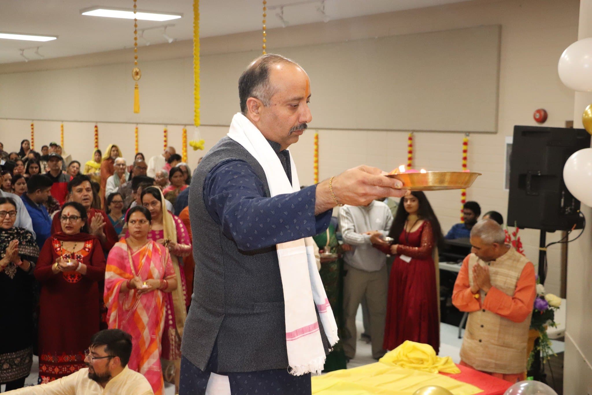 A community leader offers the aarti thali as devotees hold lit diyas