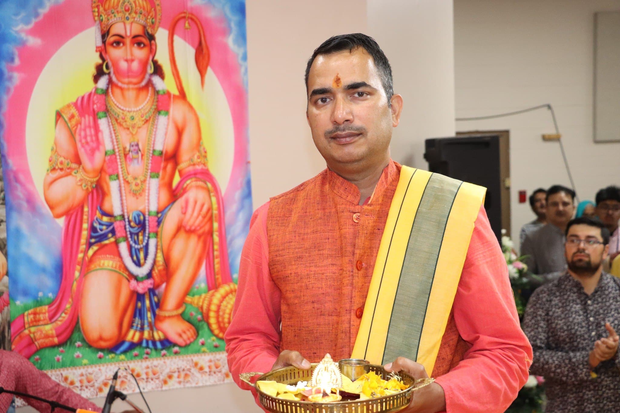 A priest holds the aarti thali before a portrait of Lord Hanuman