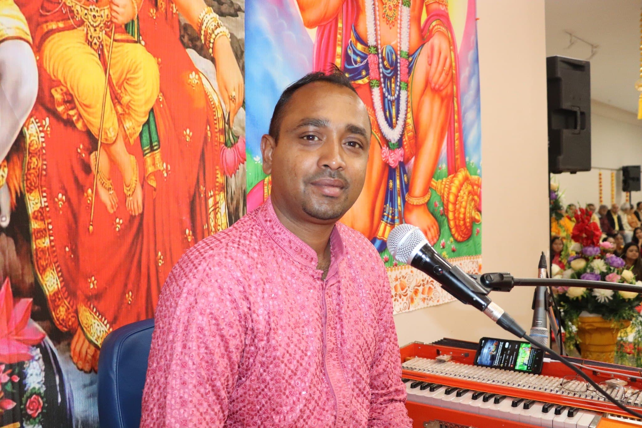 A singer plays the harmonium in front of a deity backdrop