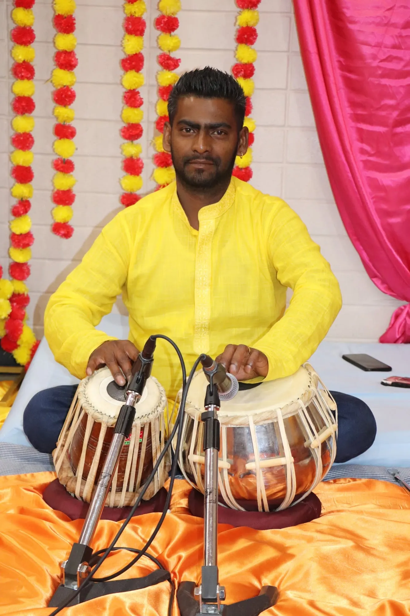 A musician in yellow playing the tabla on stage