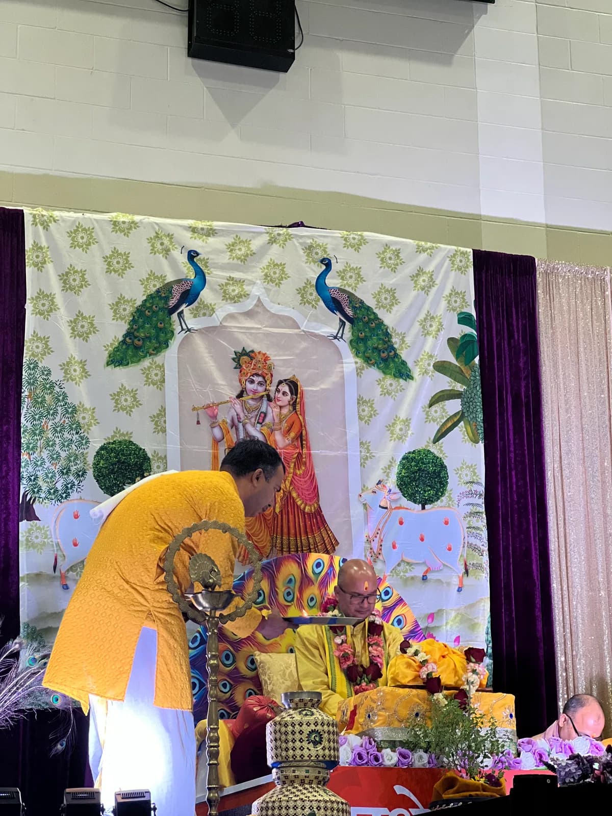 A priest prepares the offerings before the Radha–Krishna backdrop