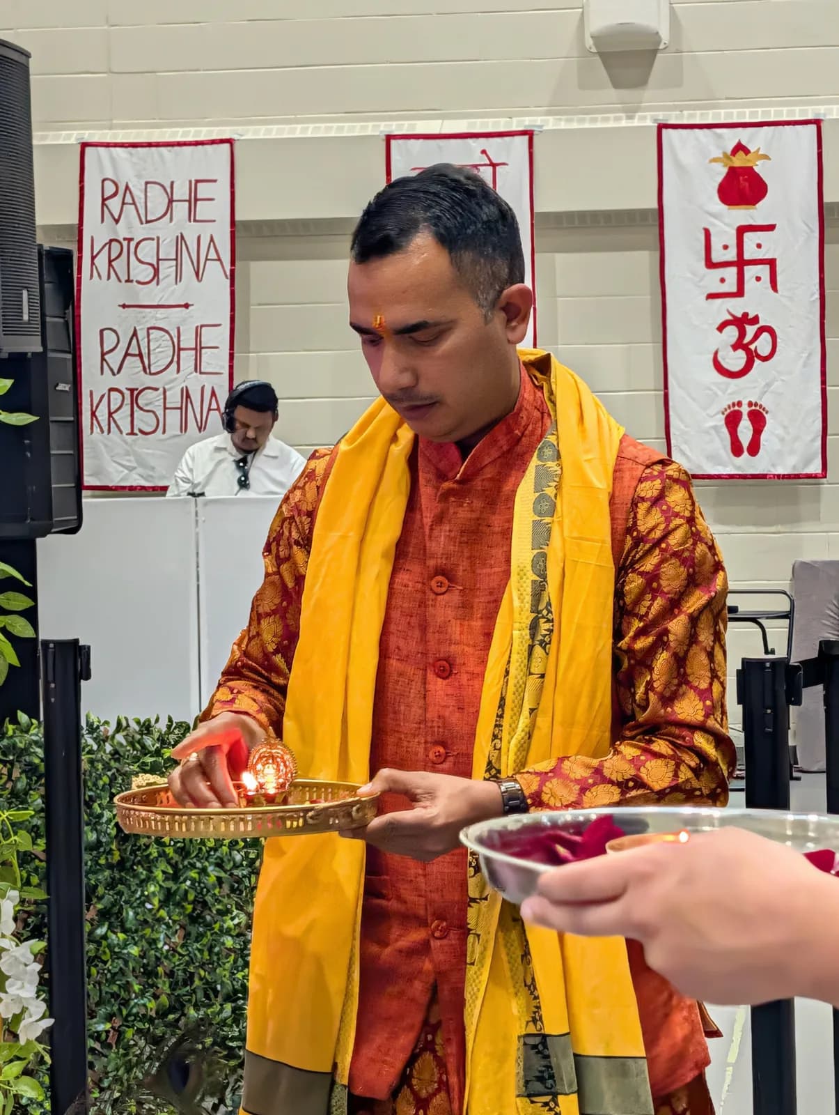 A young volunteer offers aarti before the Radhe Krishna banner