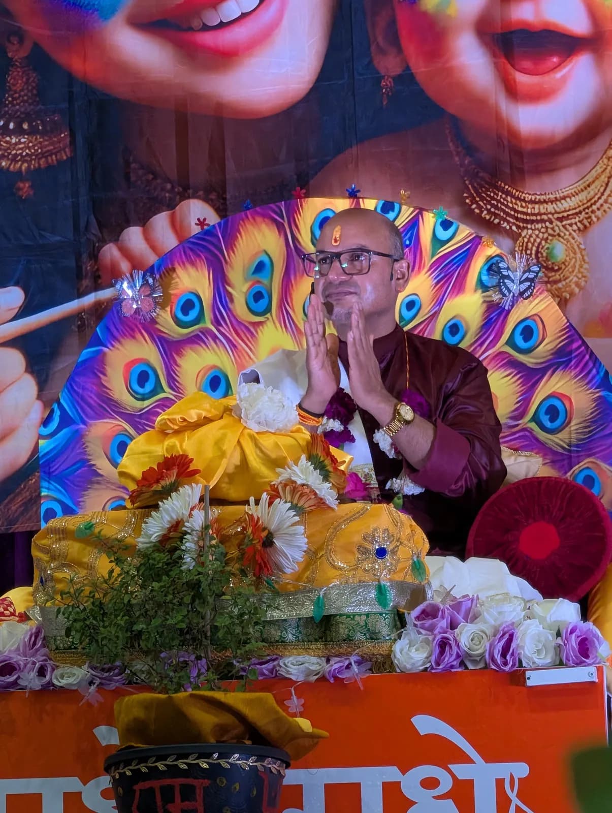 The Katha Vyas offers aarti before the peacock backdrop