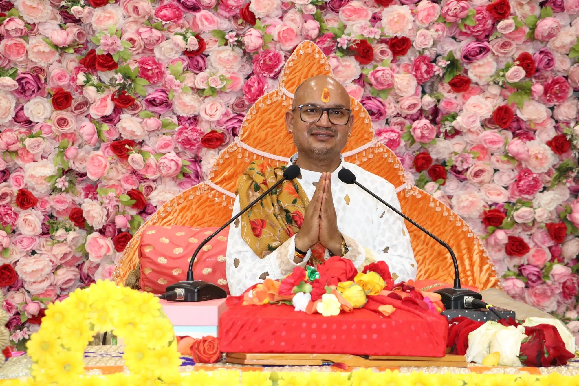 The Katha Vyas seated before a floral backdrop with folded hands